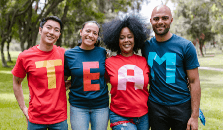 Four people standing side-by-side wearing matching t-shirts that spell out the word team
