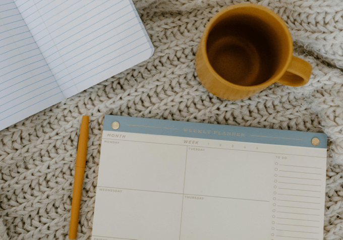 Weekly planner pad, a yellow pen and an empty mustard-yellow mug