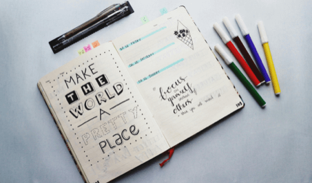 An open notebook surrounded by colorful pens