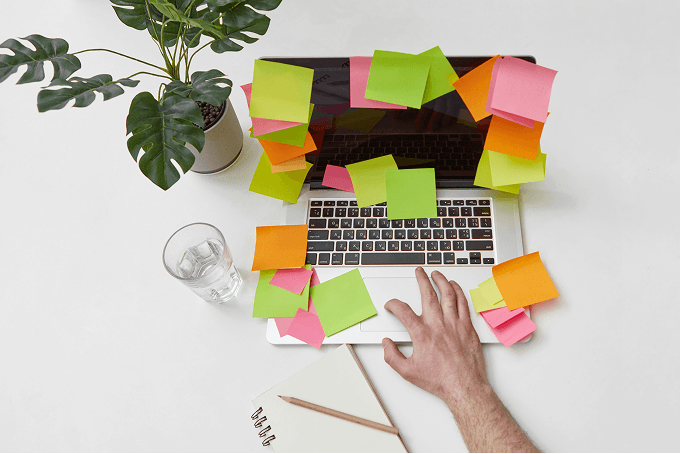 A hand rests on the trackpad of a laptop covered in colorful sticky notes