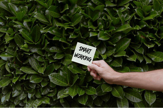 A hand holds a note with smart working written on it next to a large bush