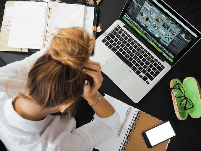 A woman sits next to a laptop and puts her hands on her head