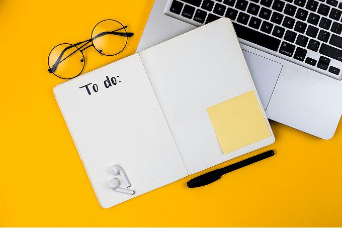 An open notebook near glasses, earphones, and a laptop