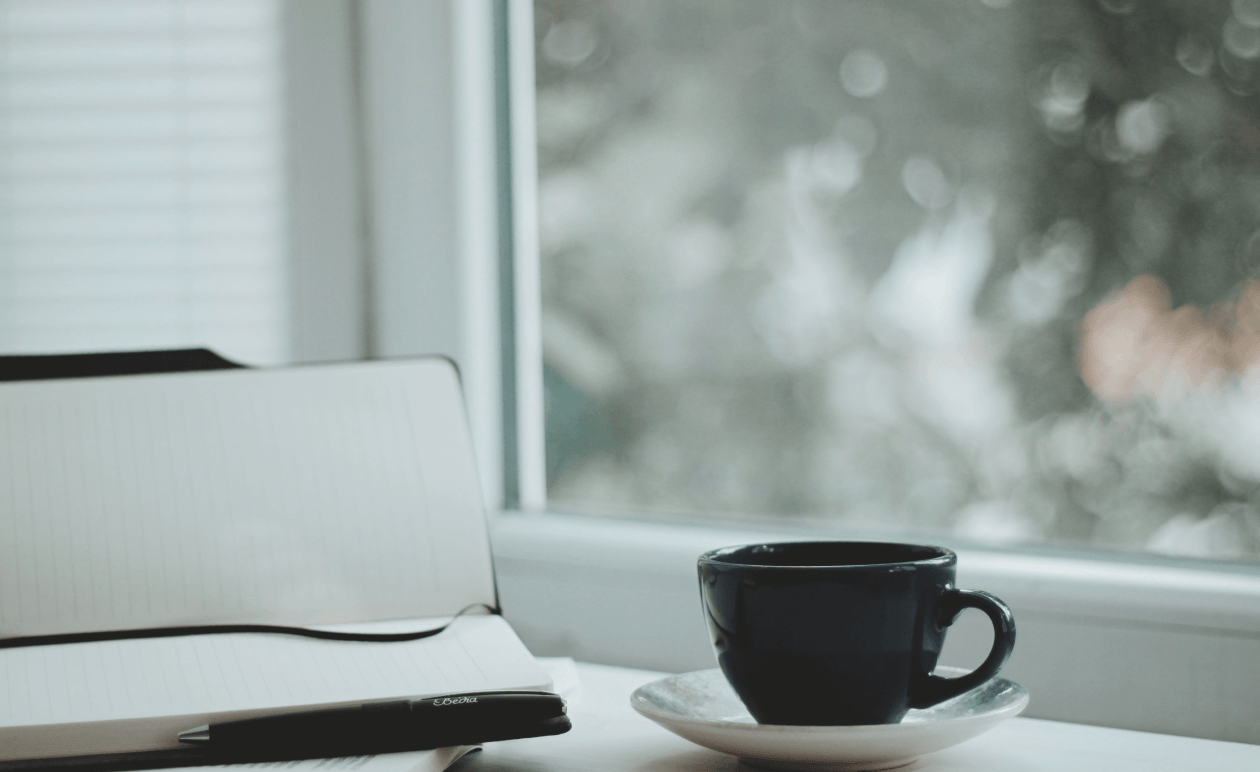 Notebook beside a pen and a cup of coffee